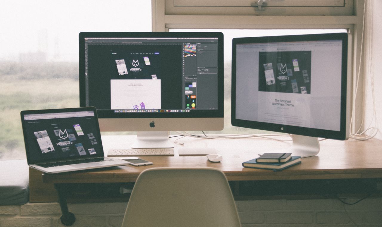 A modern, polished workspace with several monitors, a laptop, and a smartphone, highlighting a web design project.